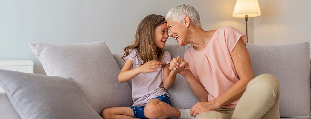 Image of senior woman sitting on couch, talking, holding hands, and laughing with a young girl